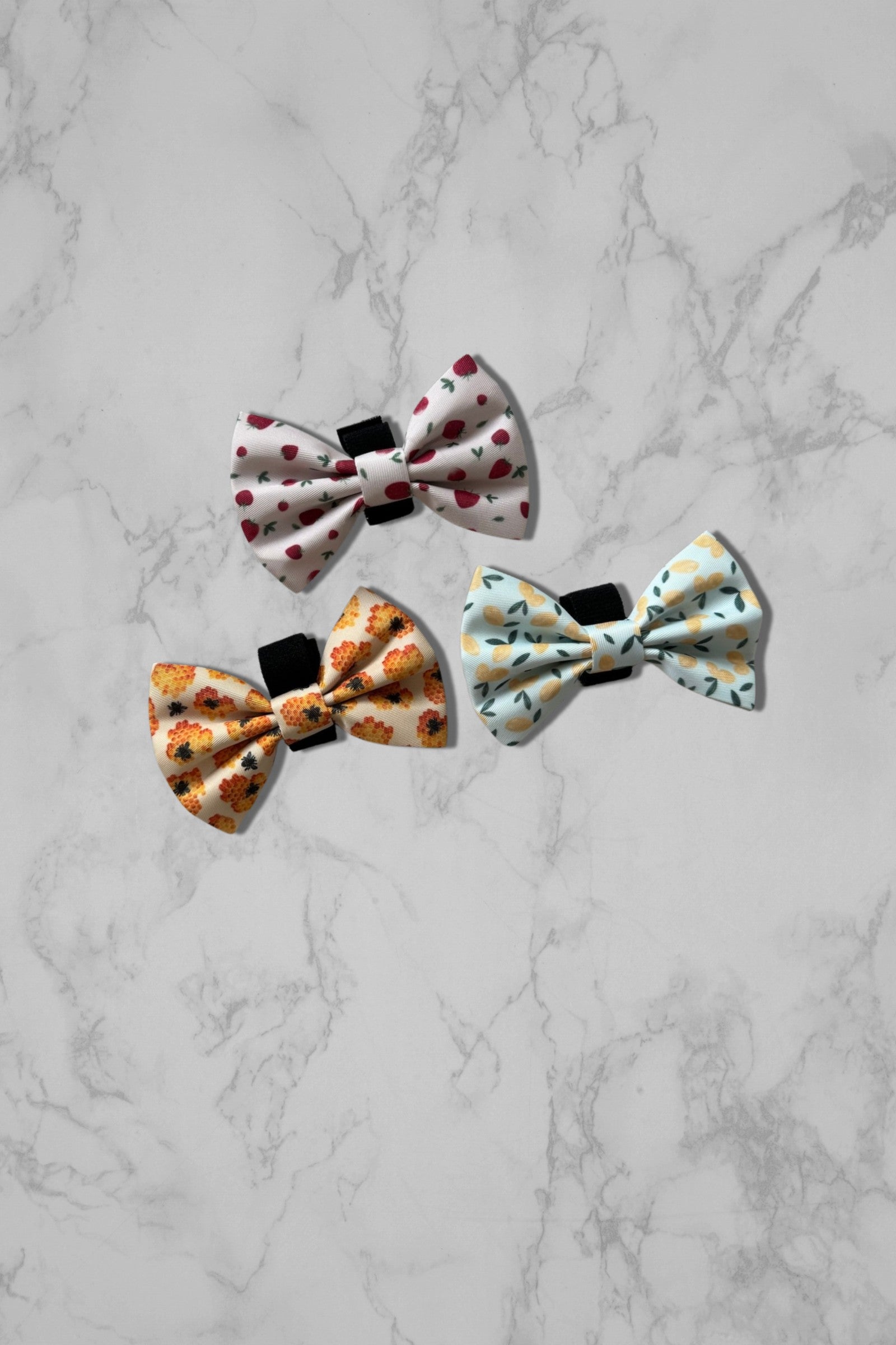 Pink bow tie, blue bow tie, and yellow dog bow tie on marble surface