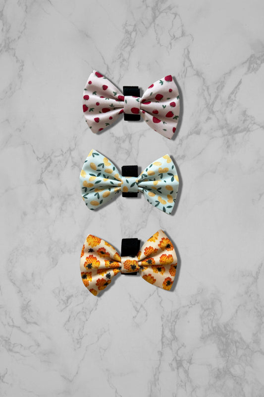 Pink bow tie, blue bow tie, and yellow dog bow tie on marble surface